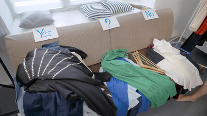 stylist is sorting clothes and putting in three heap, yes, no and unknown on couch in room of modern flat