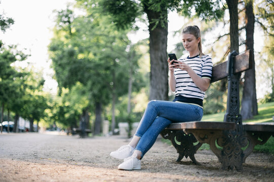 Woman text messaging on smart phone while sitting in public park