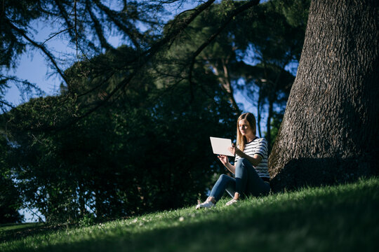 Woman using digital tablet while sitting on grass in public park