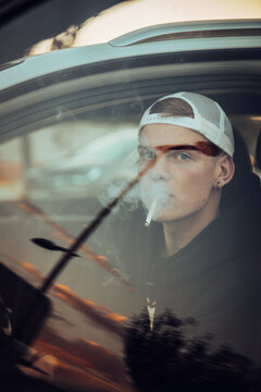 Young man smoking cigarette in car sen through window