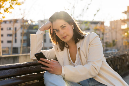 Thoughtful female entrepreneur holding smart phone while sitting on bench