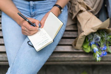 Midsection of woman writing in note pad sitting on bench