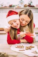 Mom hugs her daughter for helping her decorate the gingerbread cookies.