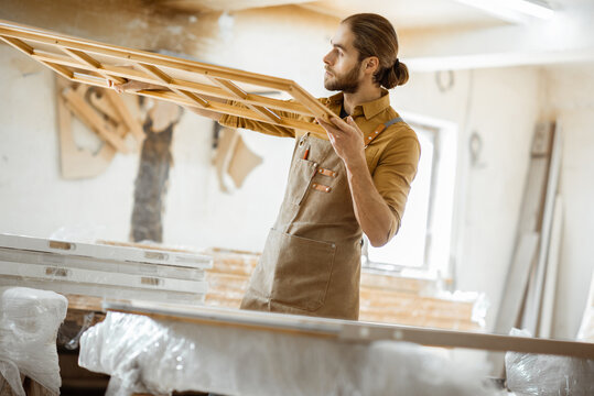 Handsome carpenter checking the quality of the window frame before the paint at the carpentry workshop