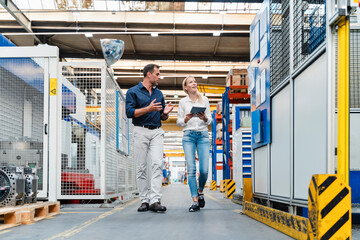 Female and male colleagues discussing while walking in factory