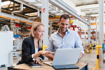 Smiling businessman and female entrepreneur using laptop at factory