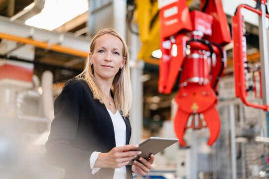 Smiling businesswoman holding digital tablet standing in industry