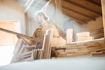 Carpenter or warehouse worker choosing raw wood material for the work at the sunny carpentry storage