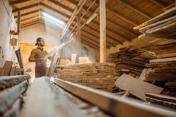 Carpenter or warehouse worker choosing raw wood material for the work at the sunny carpentry storage