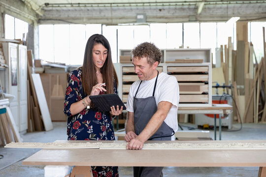 Interior designer showing digital tablet to carpenter while standing at workshop