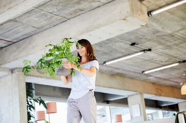 Mature woman carrying potted plant while standing at home