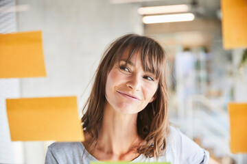 Brown hair mature woman looking at adhesive notes stick on glass material