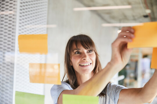 Woman smiling while sticking sticky notes on glass material