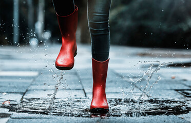 Girl wearing rubber boots splashing water while jumping in puddle on footpath