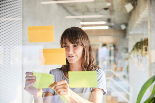Smiling mature woman sticking adhesive notes on glass material
