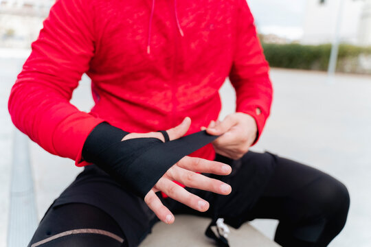 Sportsman tying boxing wrap while sitting on retaining wall