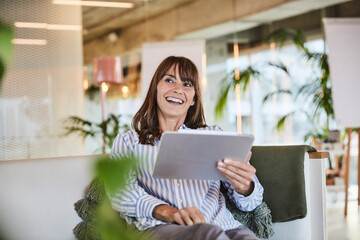 Happy woman using digital tablet while sitting at modern home