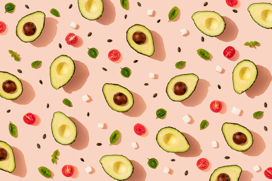 Pattern of halved avocados and cherry tomatoes, pumpkin seeds, basil and pieces of cheese