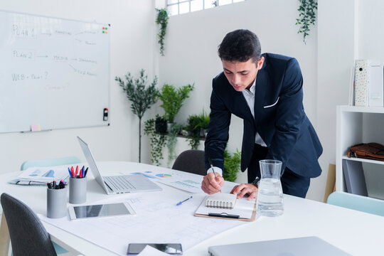 Handsome entrepreneur writing in diary while planning strategy at office desk