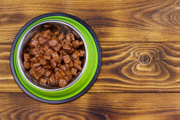 Canned food for cats or dogs in green metal bowl on wooden floor. Top view