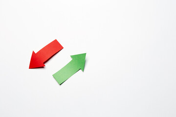 Two opposite direction right-up/left-down arrows, cutted from the red and green paper on the white plain paper background