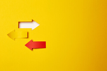 Three different direction left/right arrows, cutted from the yellow and red paper on the yellow paper background one made as an arrow shaped hole in the background with white paper underlay