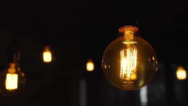 Big vintage incandescent light bulbs hanging in the dark room. Decorative antique edison light bulbs with straight wire. Inefficient filament light bulbs waste electricity. Warm white, dimmable, led