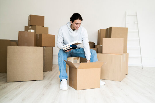 Young man removing books while unpacking box in new house