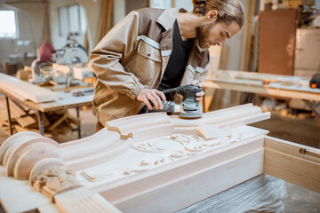 Carpenter grinding joinery product with carvings, finishing woodwork at the carpentry manufacturing