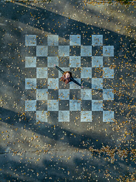 Mid adult woman with arms outstretched spinning on asphalt painted with chessboard pattern