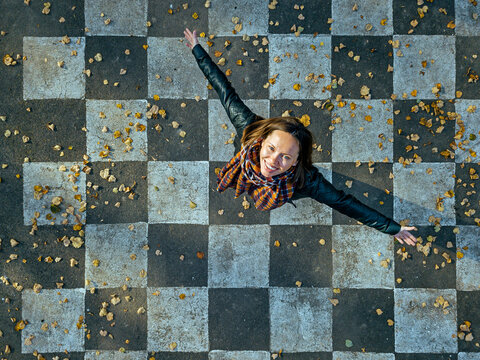 Smiling woman with arms outstretched spinning on asphalt painted with checked pattern
