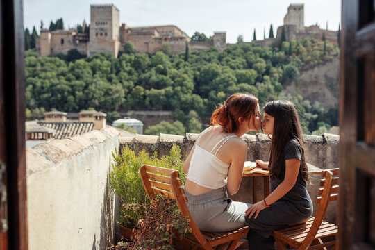 Mother and daughter kissing while sitting by table on terrace