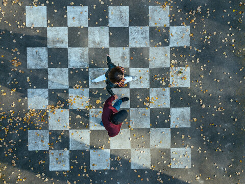 Couple holding hands while walking on chessboard painted on asphalt