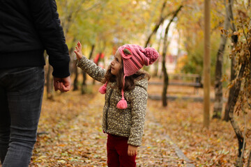 Father and daughter hiking in the forest in the autumn. The girl and her father are having fun and holding hands.