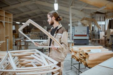 Handsome carpenter checking the quality of the window frame before the paint at the carpentry workshop