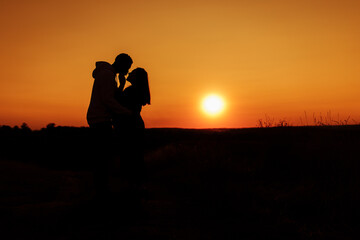 Fototapeta na wymiar Silhouettes of lovely couple, handsome man gently hug beautiful woman at sunset, enjoy tender moments, caring husband and loving wife spend time together, weekends outdoors concept