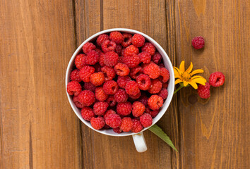 Juicy red raspberries in a white mug on a wooden table. with yellow sunflower
