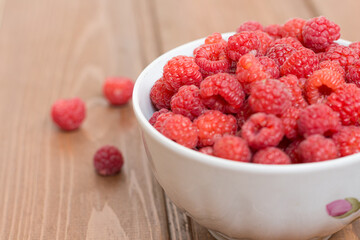 Juicy red raspberries in a white mug on a wooden table