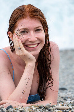 Smiling woman with gravel and sand face lying on beach