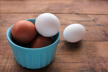 Fresh chicken eggs in a blue bowl on wooden table. View from overhead.
