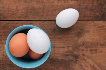 Fresh chicken eggs in a blue bowl on wooden table. View from overhead.