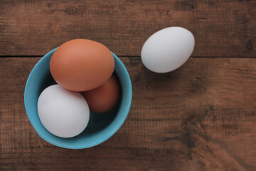 Fresh chicken eggs in a blue bowl on wooden table. View from overhead.