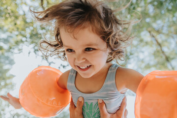 Mother's hand picking up daughter in air with swimmies at beach