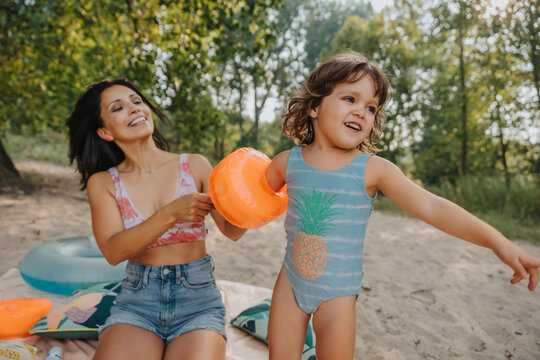 Mother putting swimmies to daughter at beach