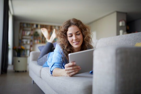 Woman using digital tablet while lying on sofa at home