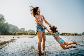 Mother whirling daughter around while standing in water at beach