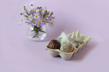 Colored eggs in a package with a light feather on the background of a bouquet of delicate flowers, pastel background, space for text