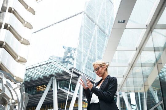 Beautiful female professional using smart phone while standing against office building at downtown district