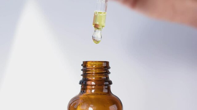 A pipette / dropper dispensing a drop of solution / medicine / vitamin / supplement on a white background