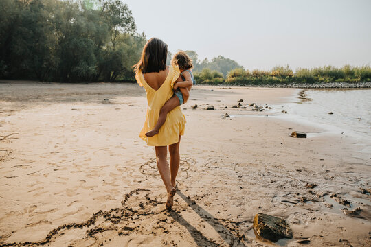 Mother carrying daughter while walking on sand at beach